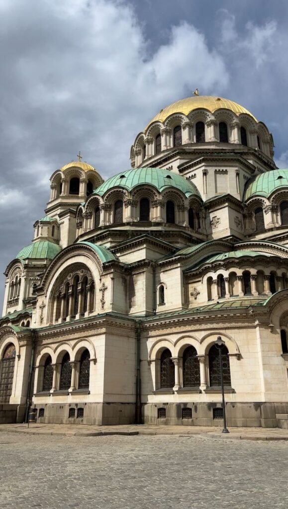 Golden and green domes of Alexander Nevsky Cathedral against a cloudy sky